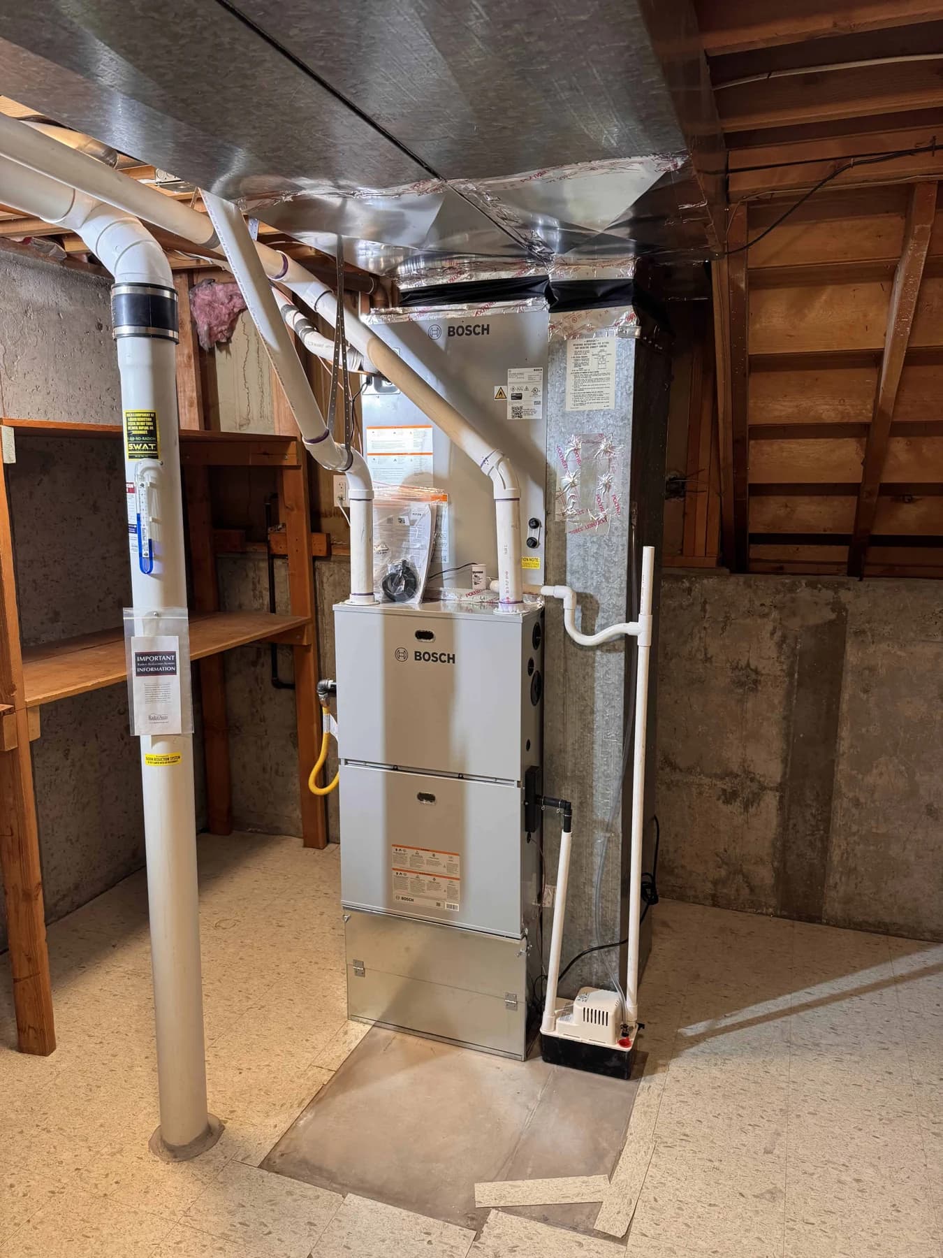Bosch indoor equipment in an unfinished basement, with a tall supply transition, white piping, adjacent structure and the approach to the cabinet visible