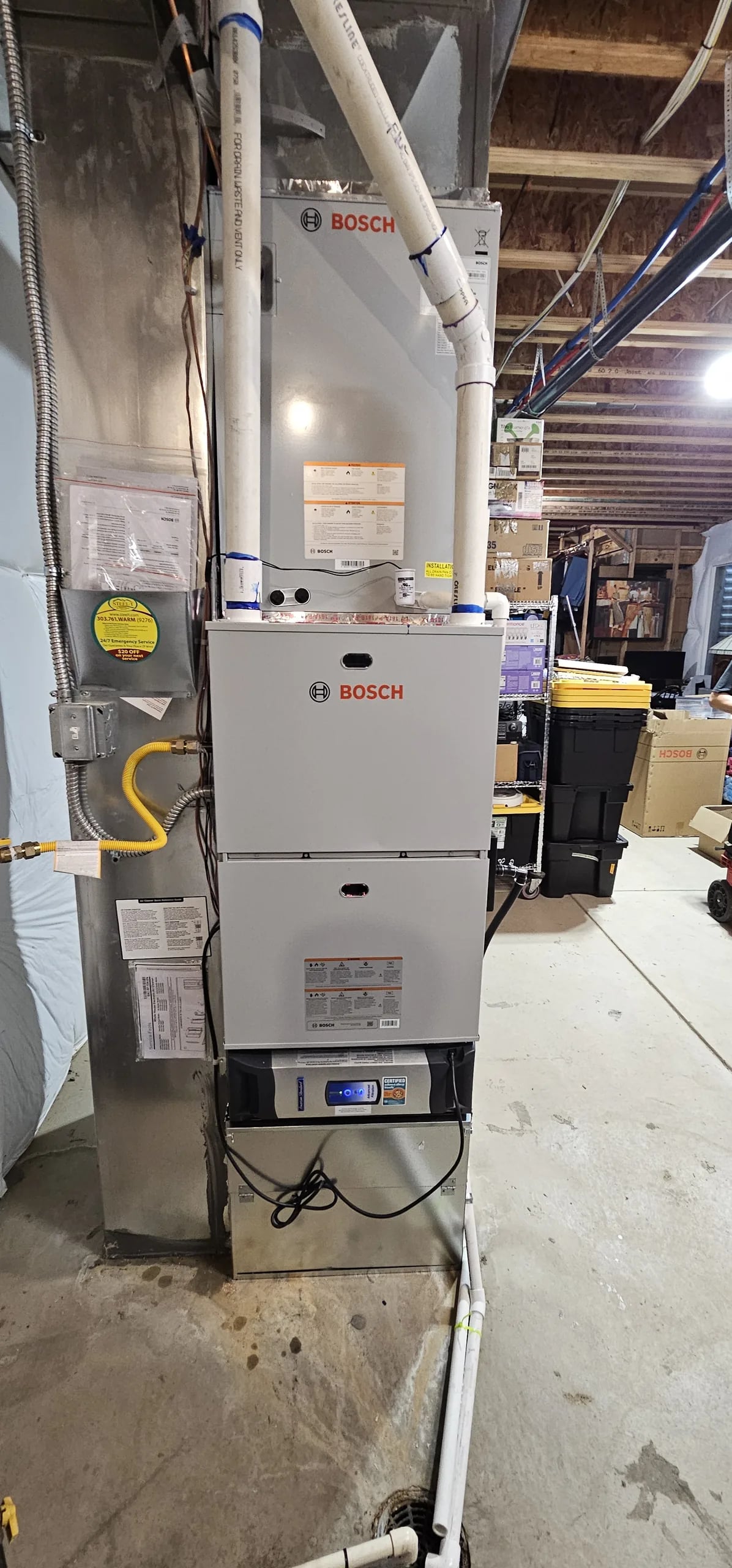 Tall Bosch furnace and coil on a garage floor with two PVC pipes running up