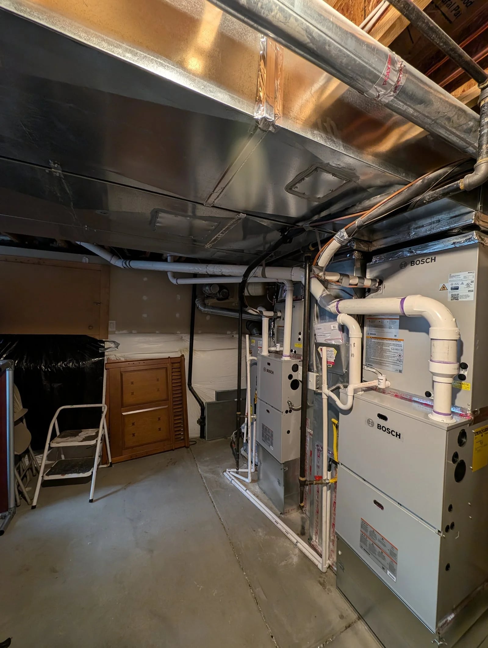 Two new Bosch furnaces side by side in a basement, with white PVC vent pipes running up into the ceiling