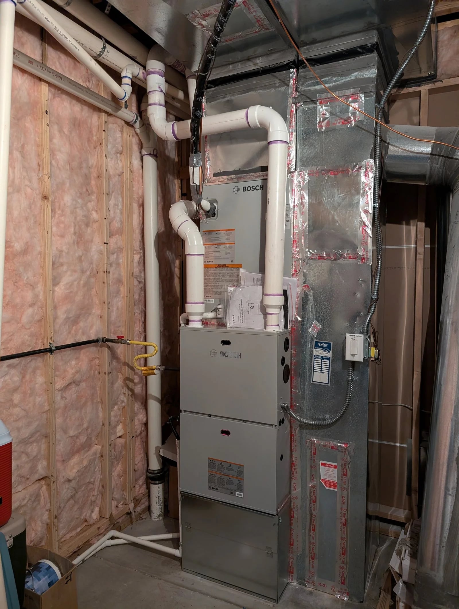A Bosch gas furnace and coil with new PVC venting against an insulated basement wall