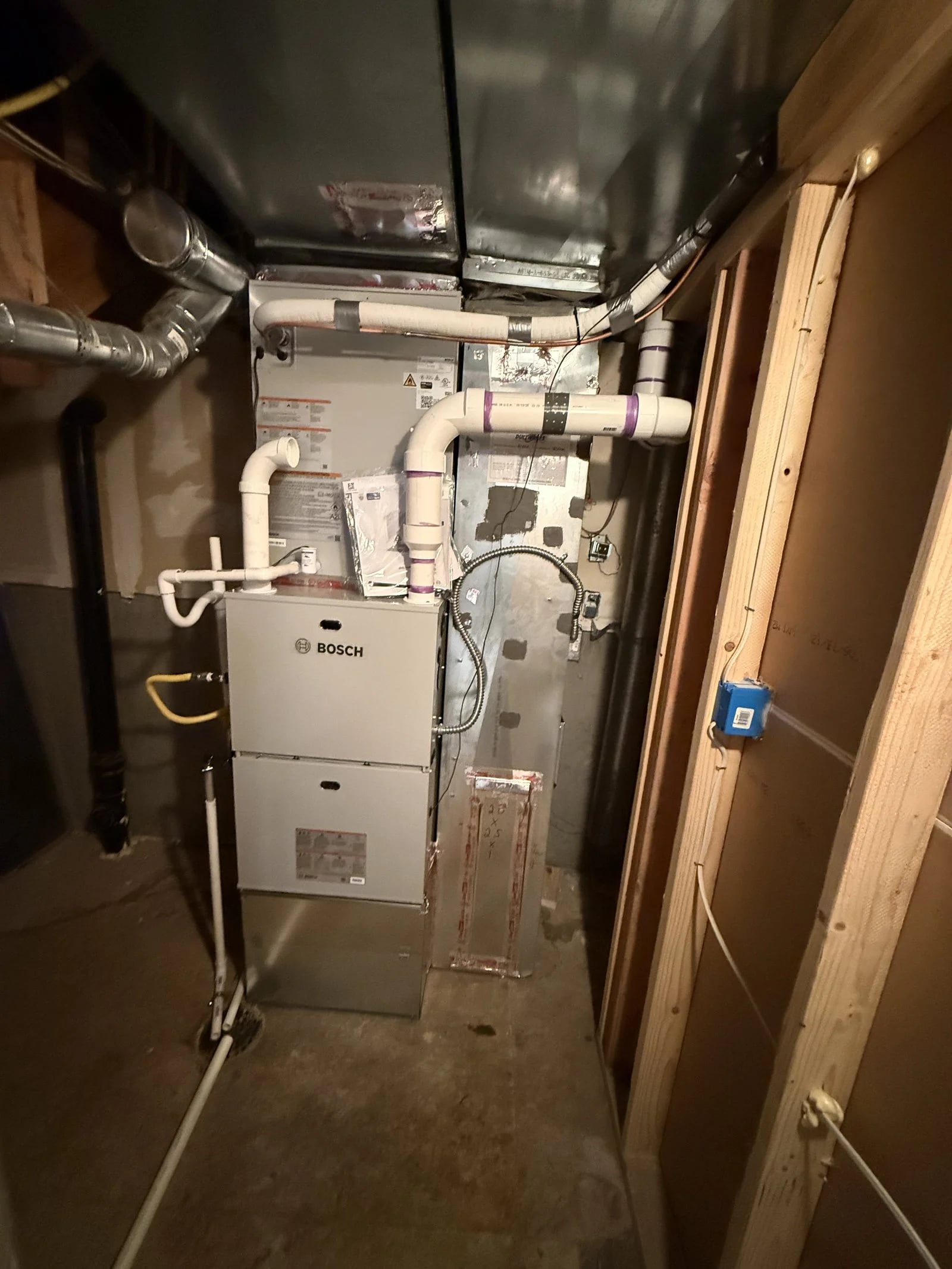 A Bosch high-efficiency furnace with white PVC intake and exhaust pipes in a basement